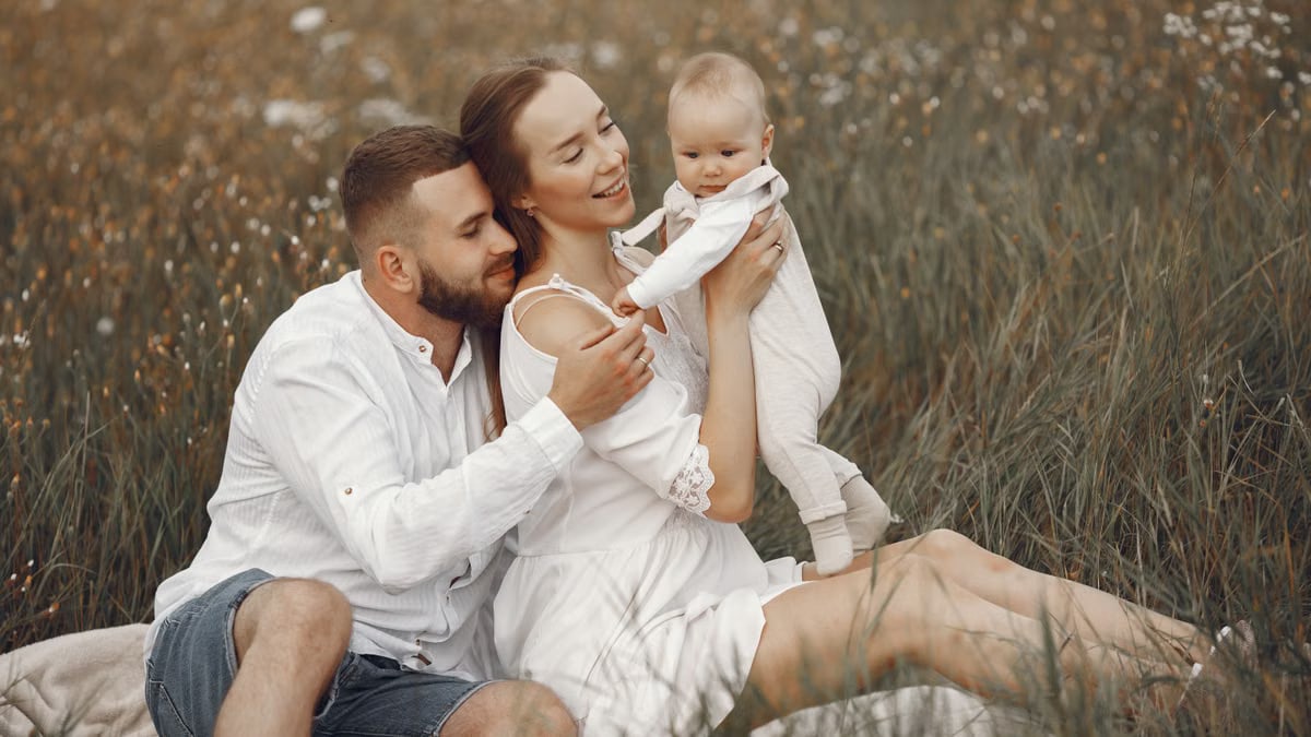A joyful family with a baby relaxing outdoors in a field during summer.